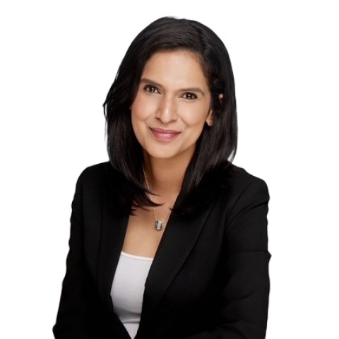 A woman with straight, shoulder-length black hair, wearing a black blazer over a white top, sits and smiles against a plain white background.